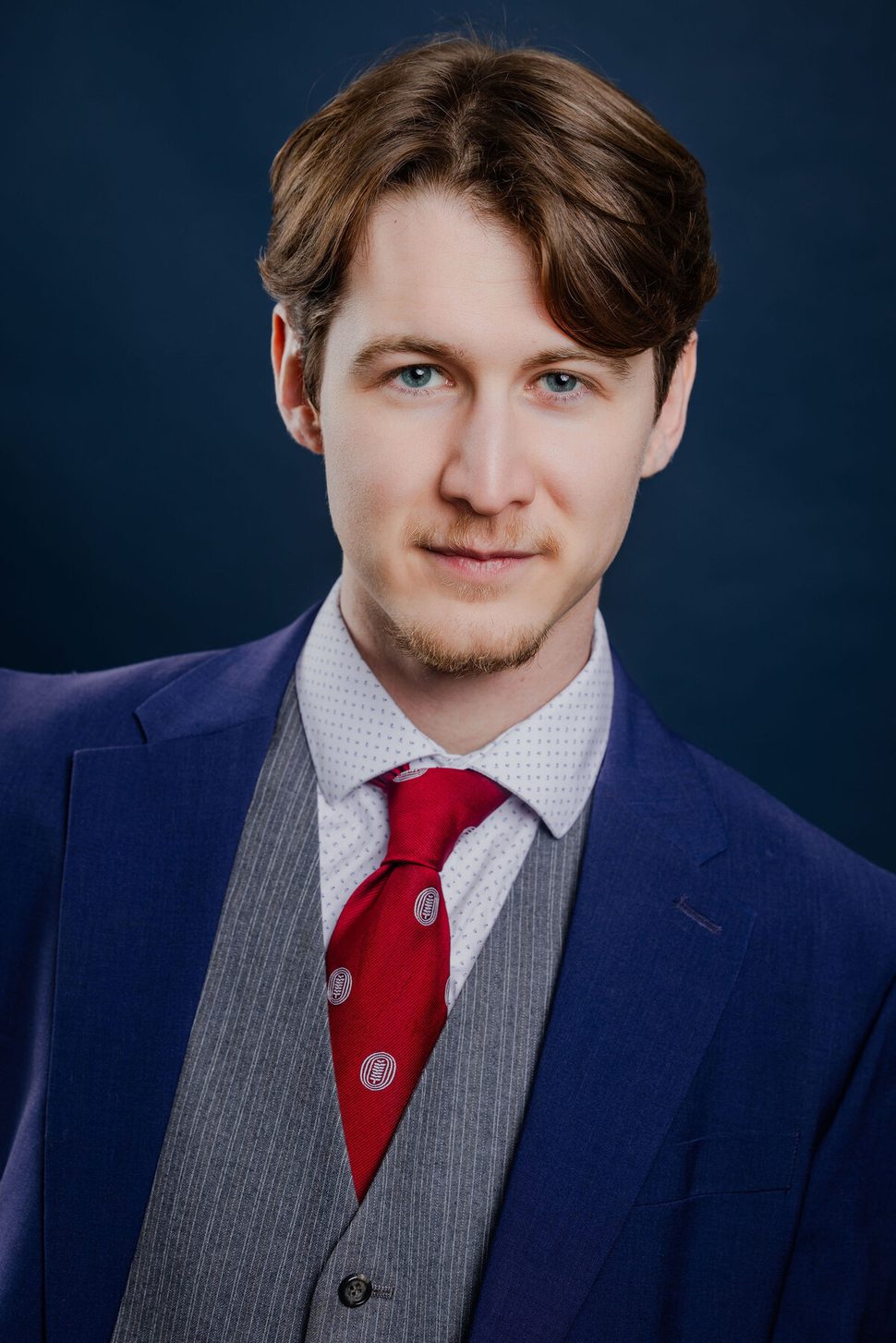 Anthony Edward, headshot — three-piece blue suit on dark navy background