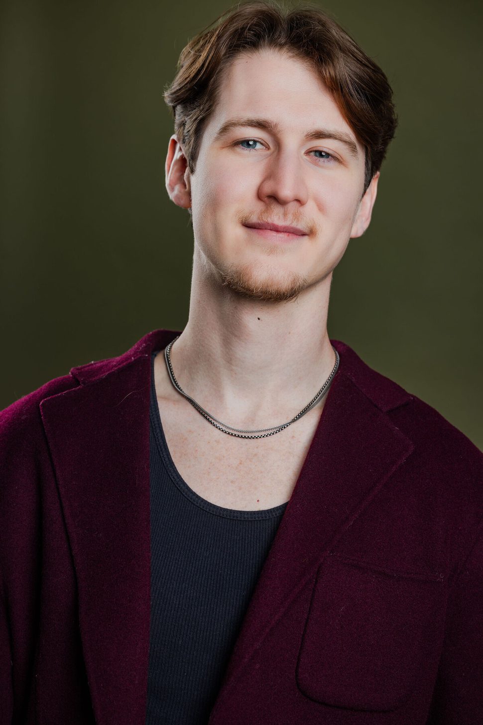 Anthony Edward, headshot — burgundy cardigan on green background